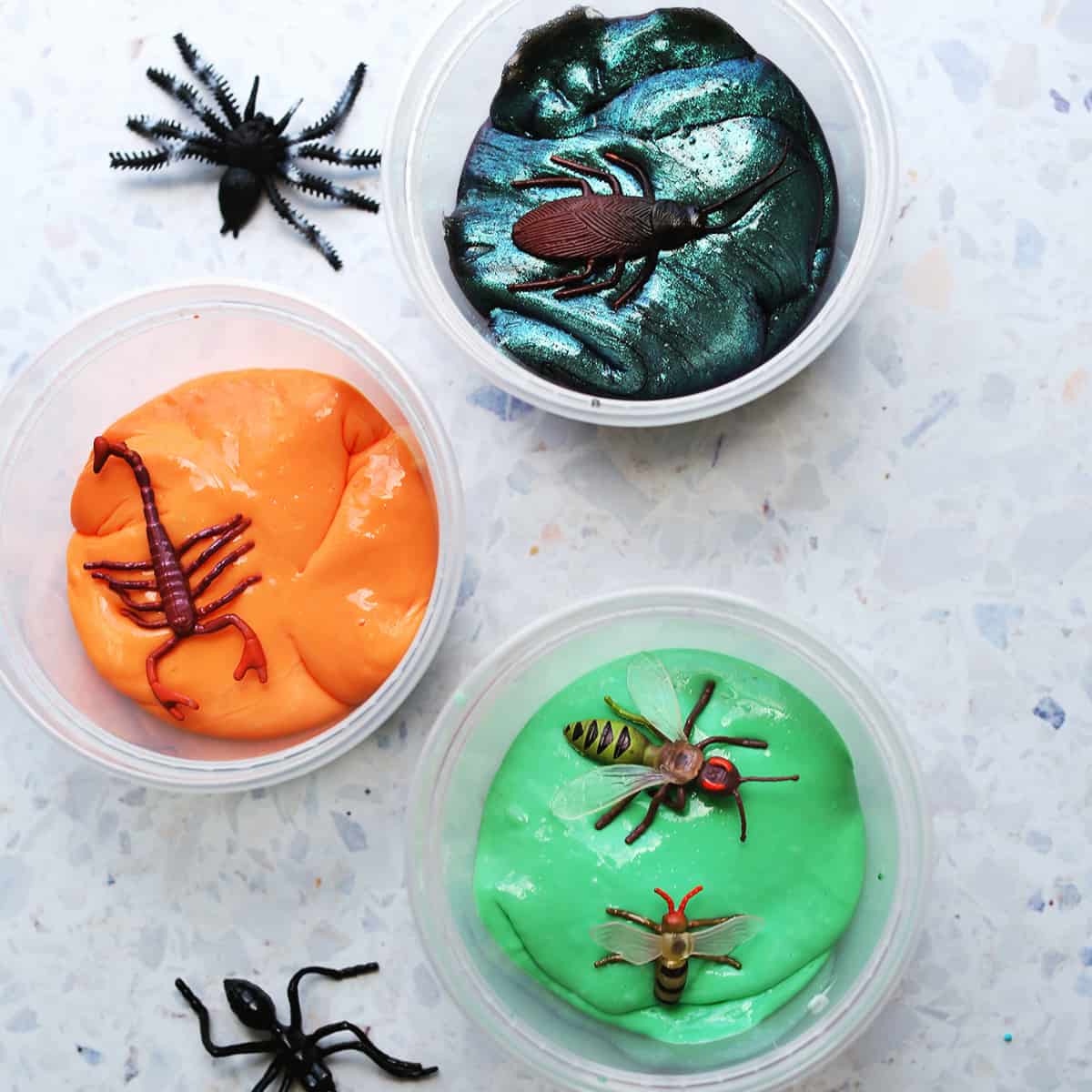 galaxy slime, orange and green slime on a counter with fake bugs.