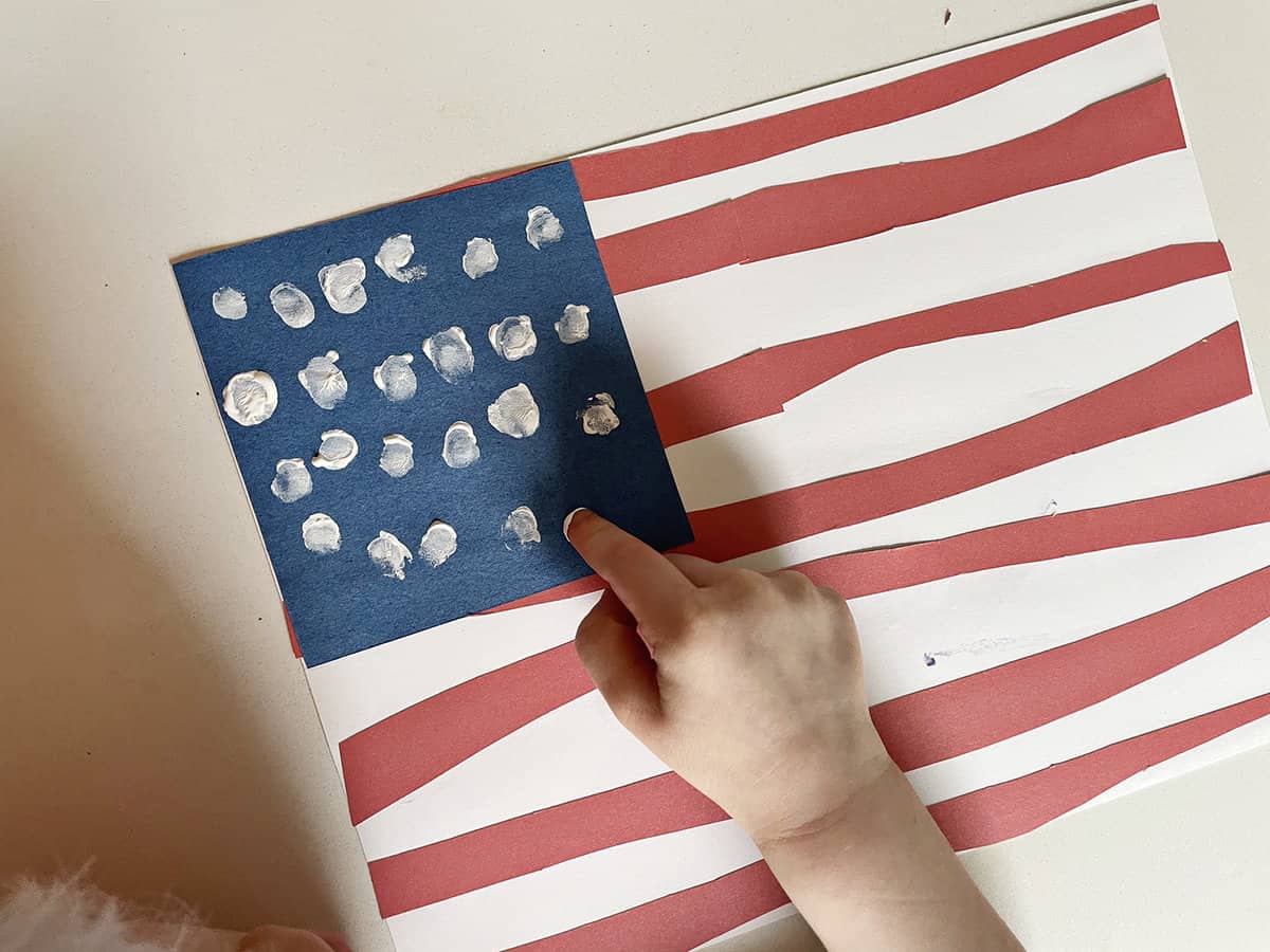 Child's fingerprint adding white dots to a blue background to make an American flag. 