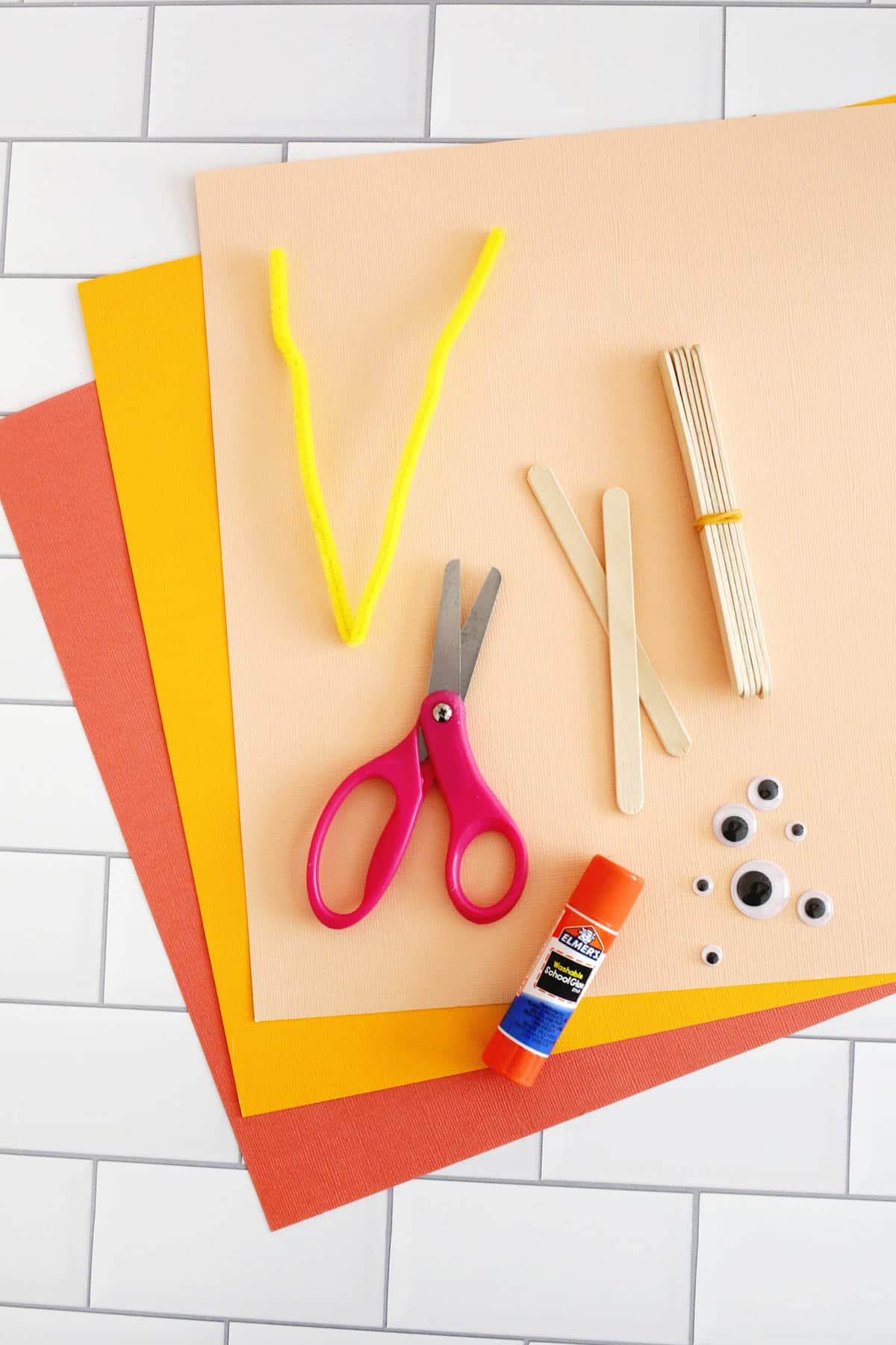 cardstock, scissors, glue, popsicle stick and googly eyes on a counter. 