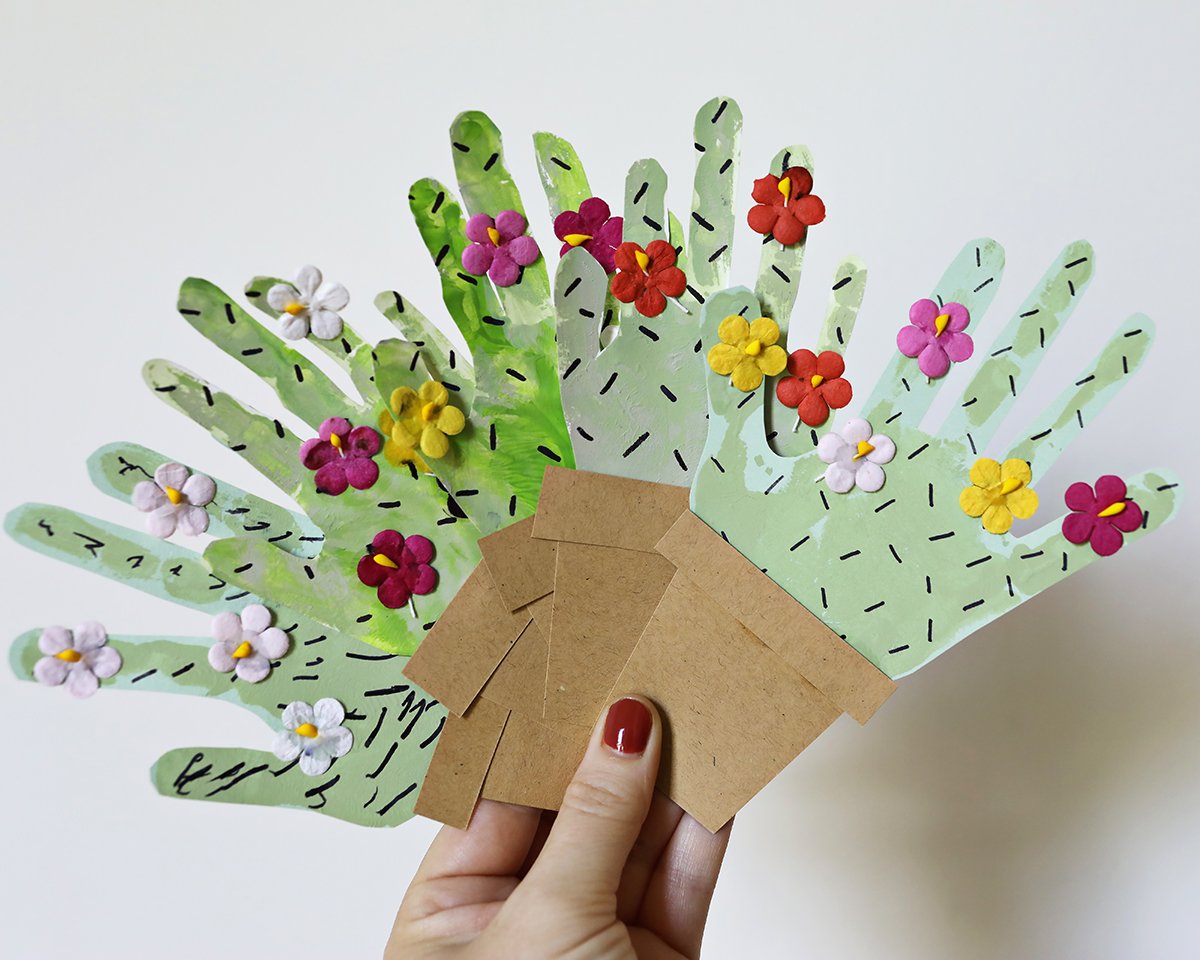 hand holding paper cactus craft made with handprints. 