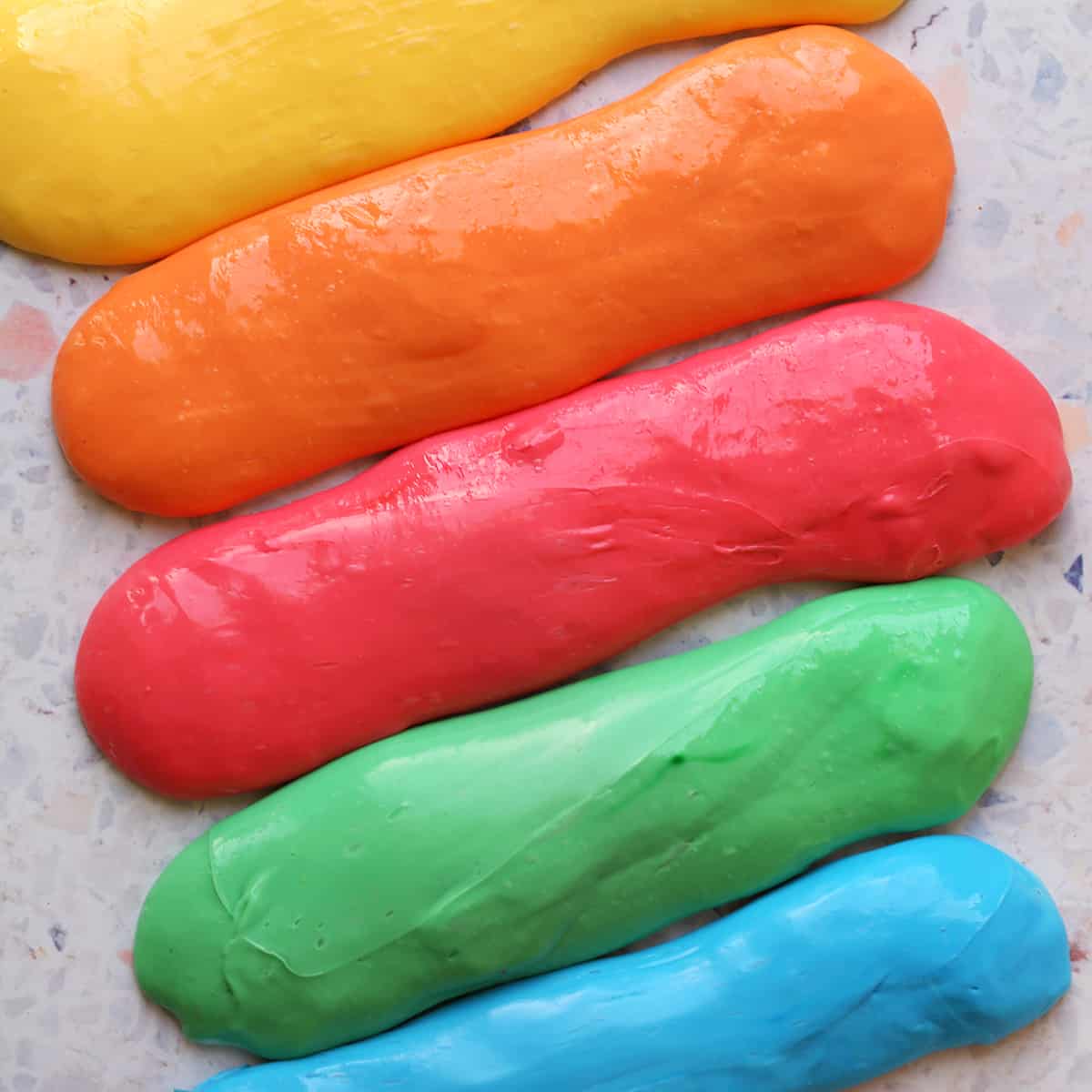 Yellow, orange, red, green and blue homemade slime sitting on the counter. 