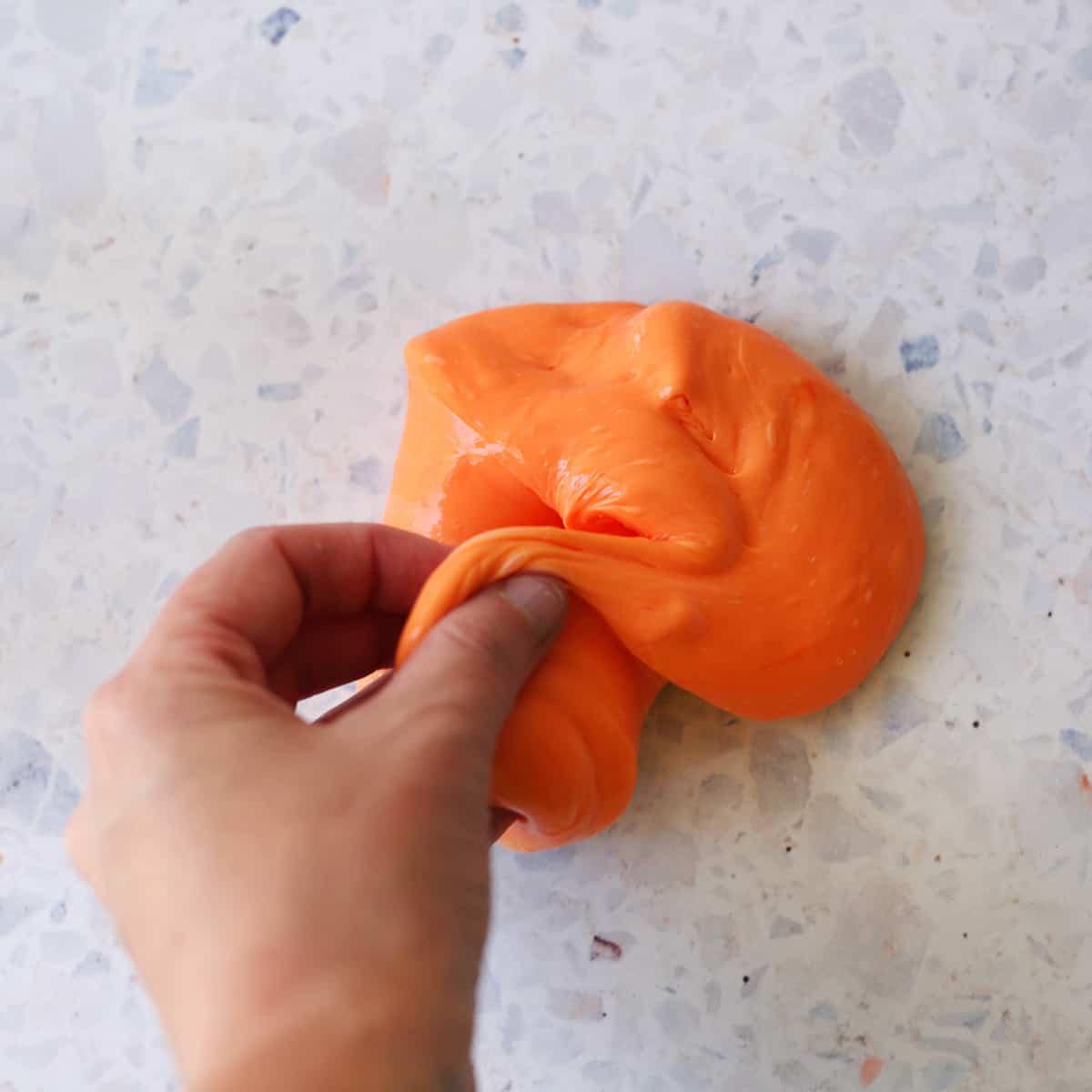 Hand pinching orange slime to show consistency. 