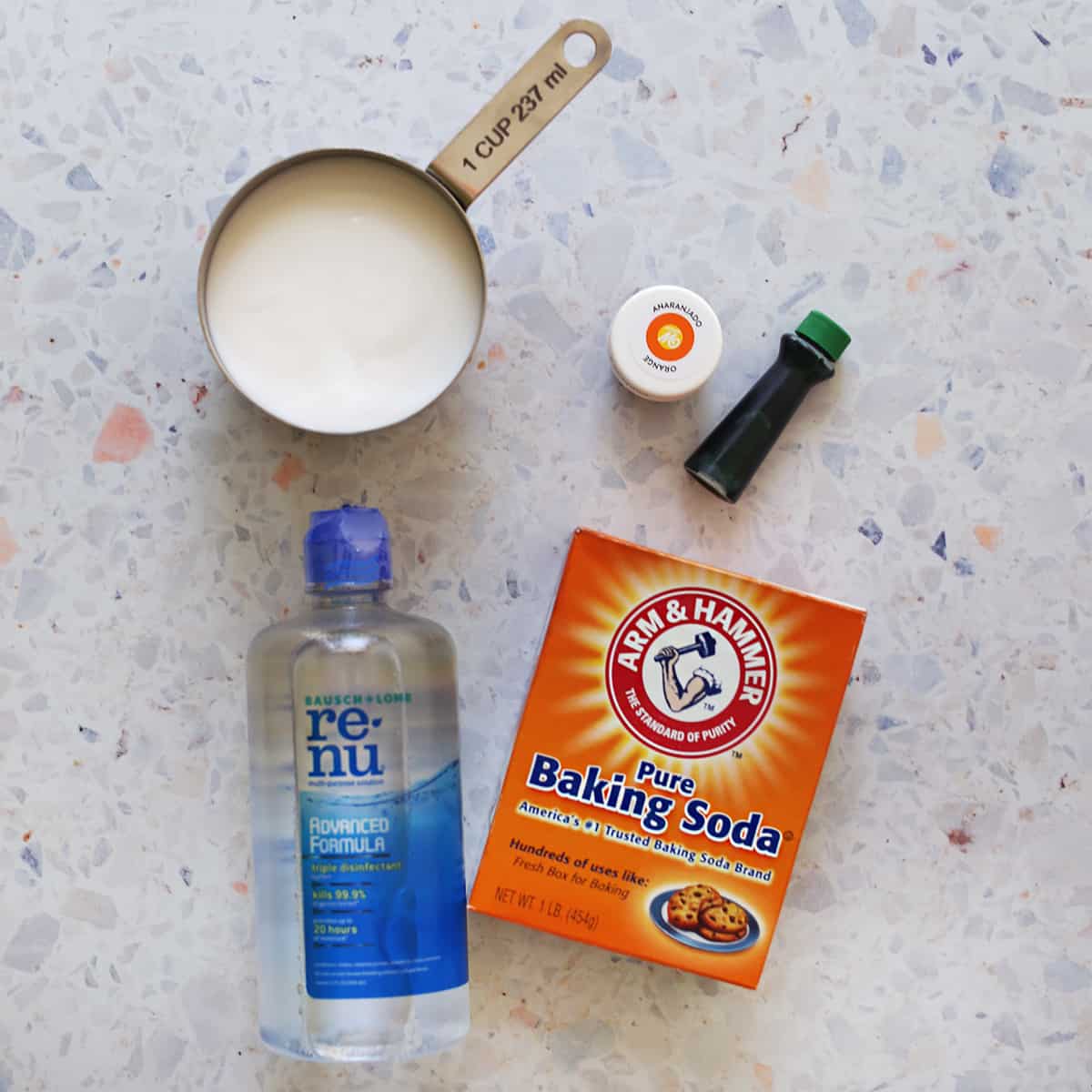 Baking soda, contact solution, glue and food coloring on a kitchen counter. 