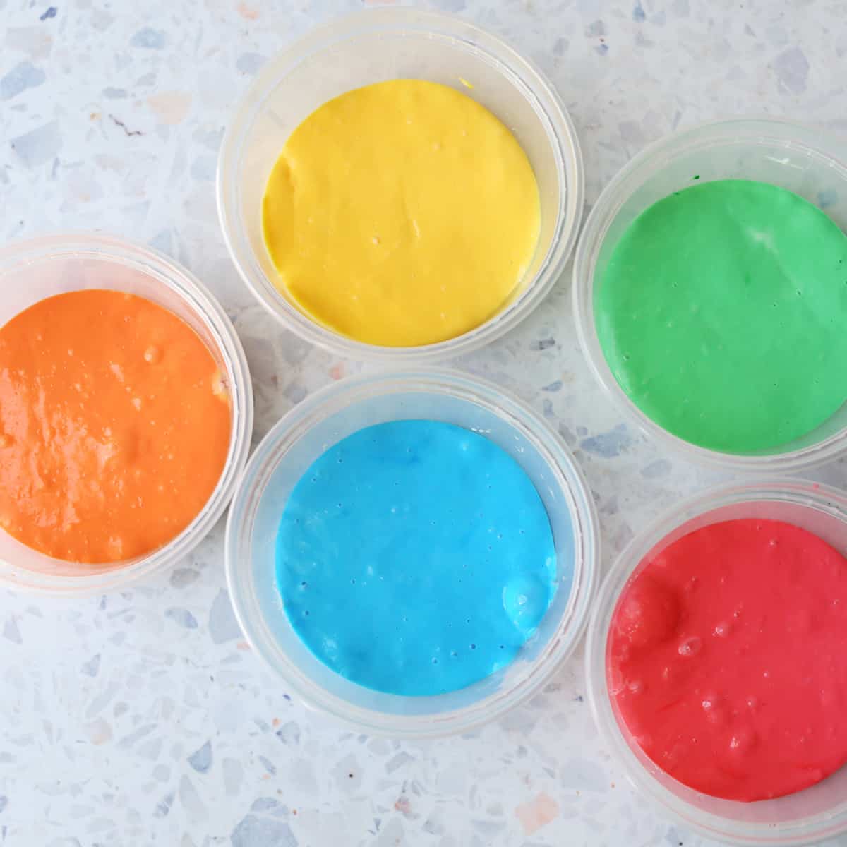 Yellow, green, orange, blue and red slime in plastic storage containers. 
