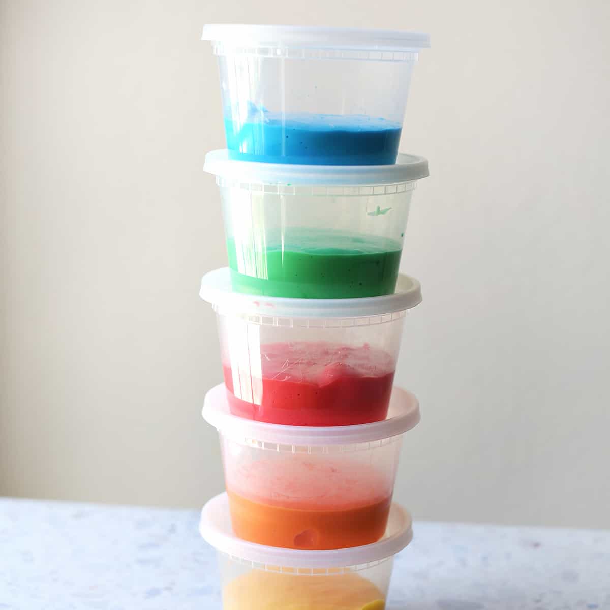 Blue, green, red, orange and yellow slime in plastic storage containers stacked on a counter. 