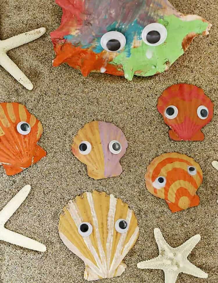seashells painted with googley eyes in sand.