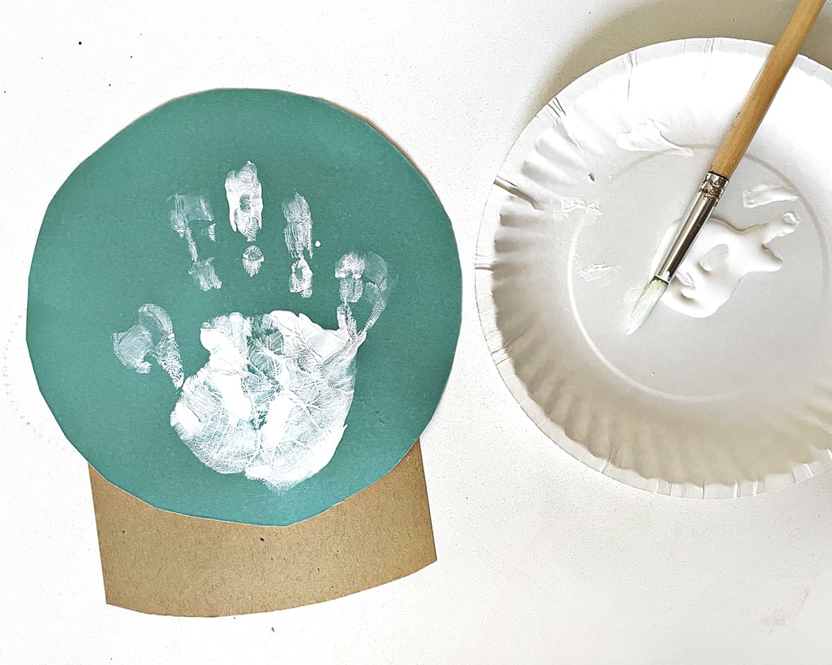 paper plate, paint brush and handprint on teal construction paper. 