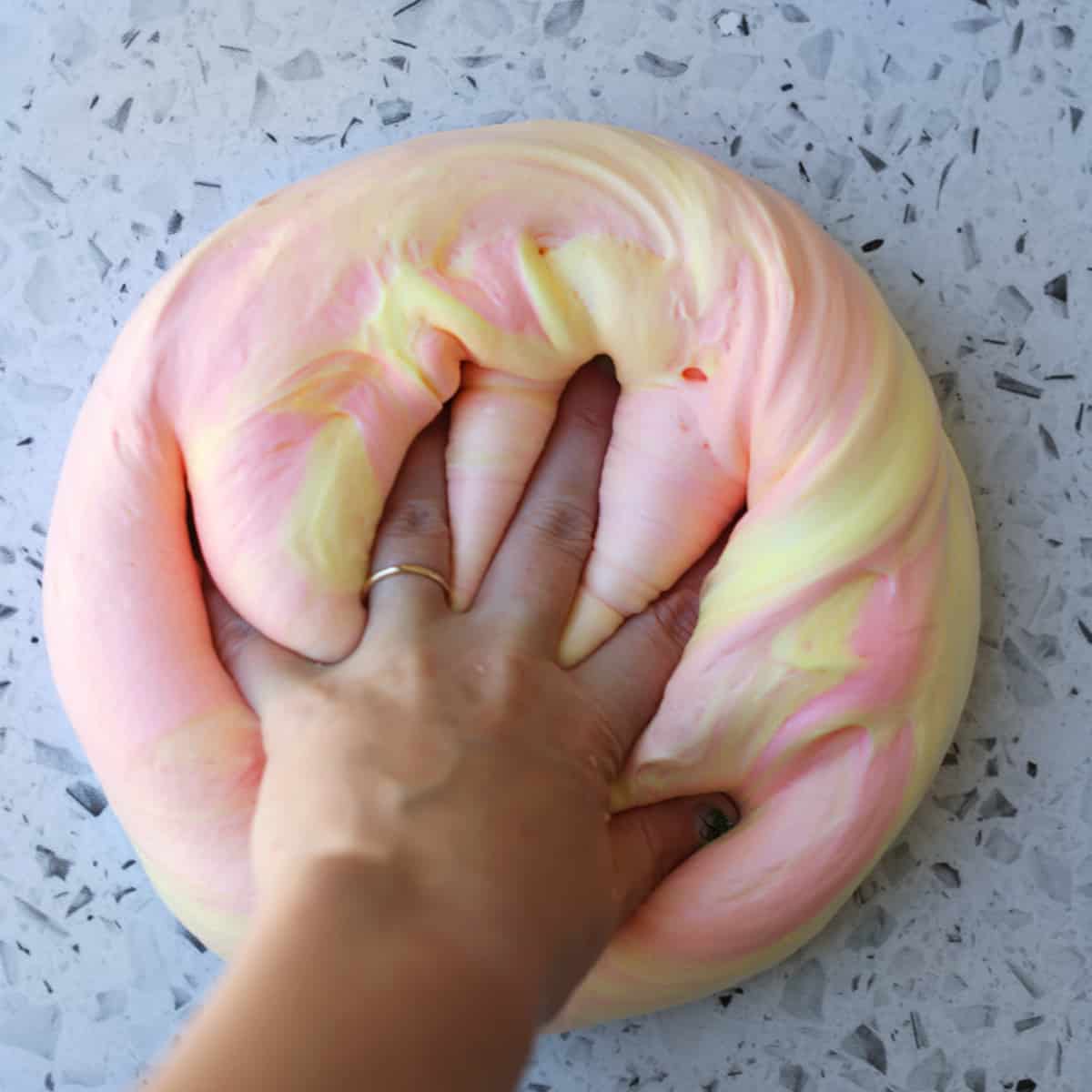 Hand kneading pink and yellow slime. 