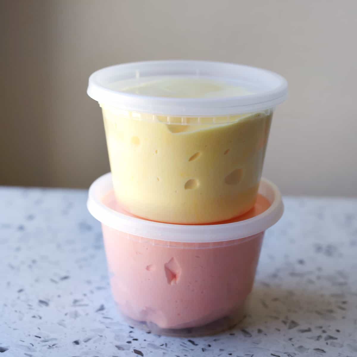 Two clear containers stacked with pink and yellow slime. 