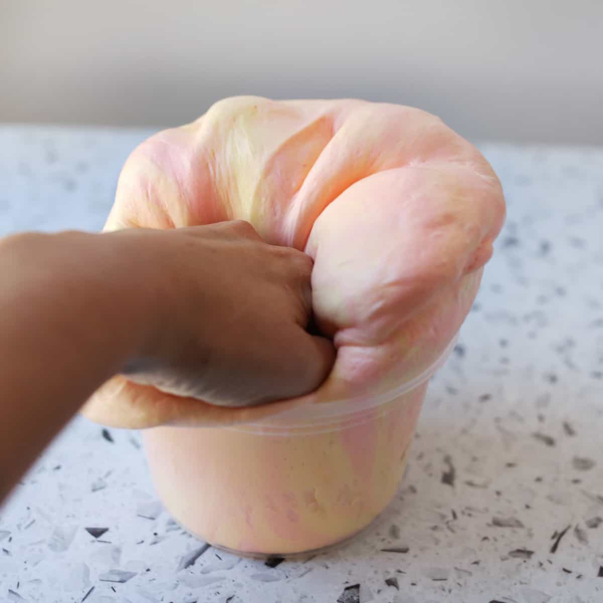 Hand kneading fluffy slime in container. 