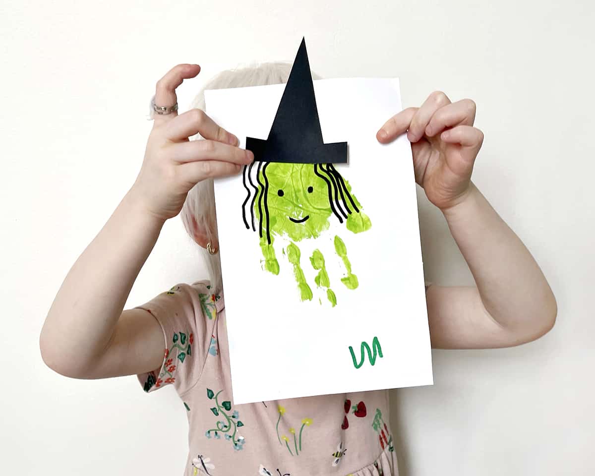 Child holding up a witch handprint craft. 