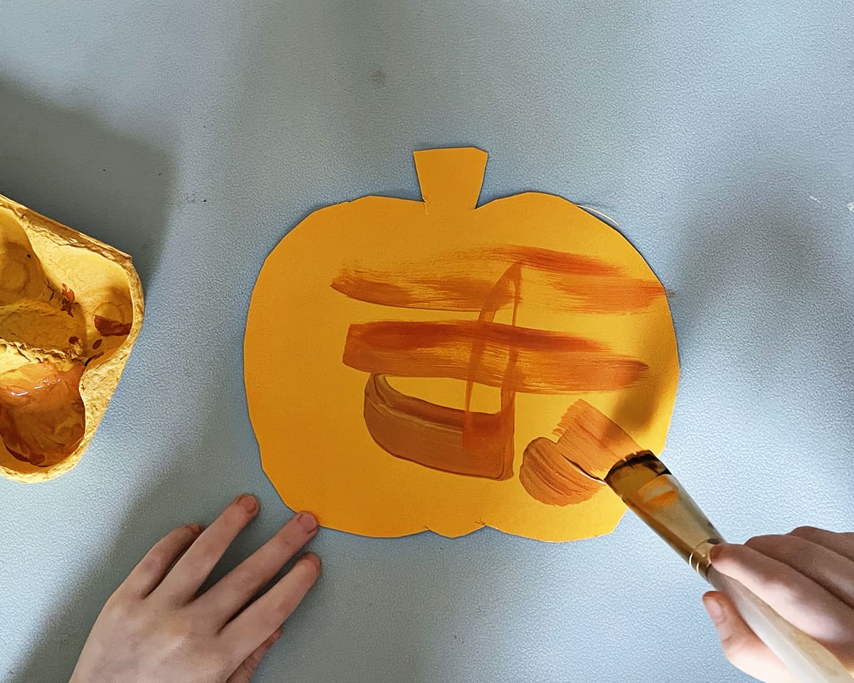 Paper pumpkin being painted by a child.