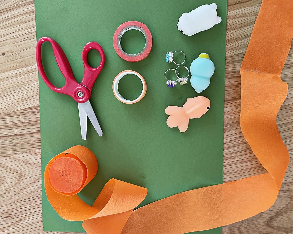 green construction paper, tape, scissors and orange crepe paper on a table.