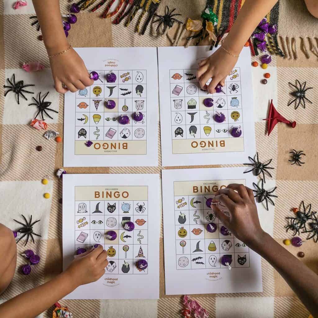 children's hands placing tokens on Halloween-themed Bingo cards.