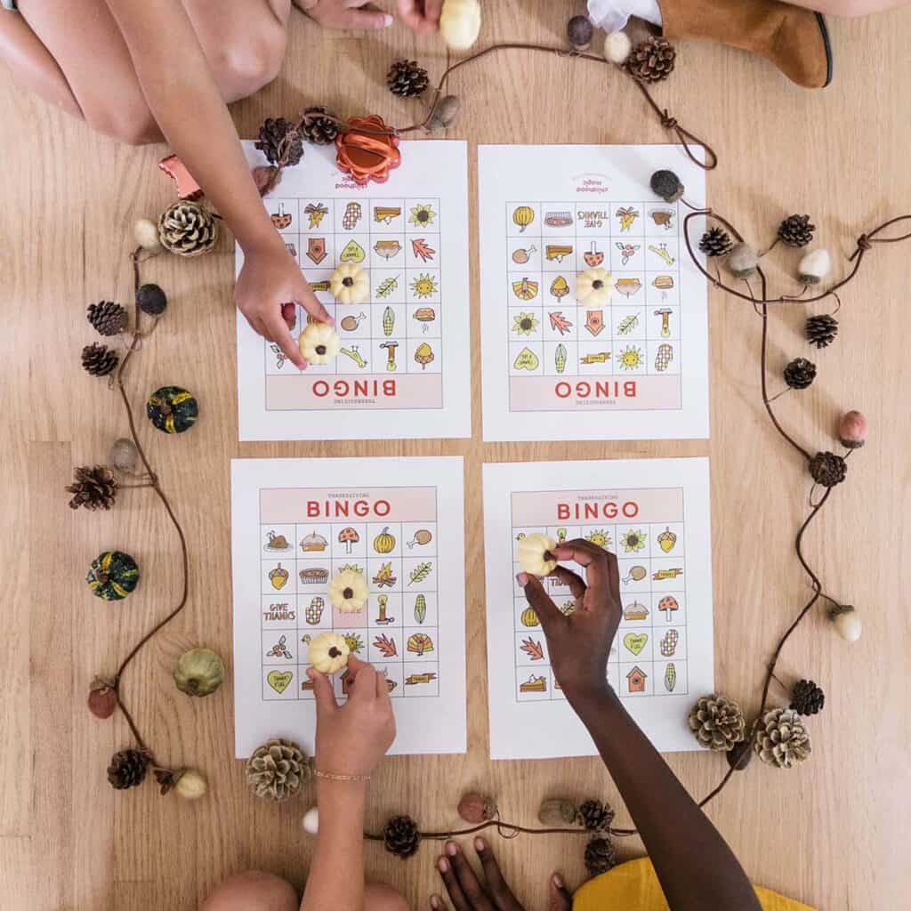children's' hands placing tokens on Thanksgiving-themed bingo cards.