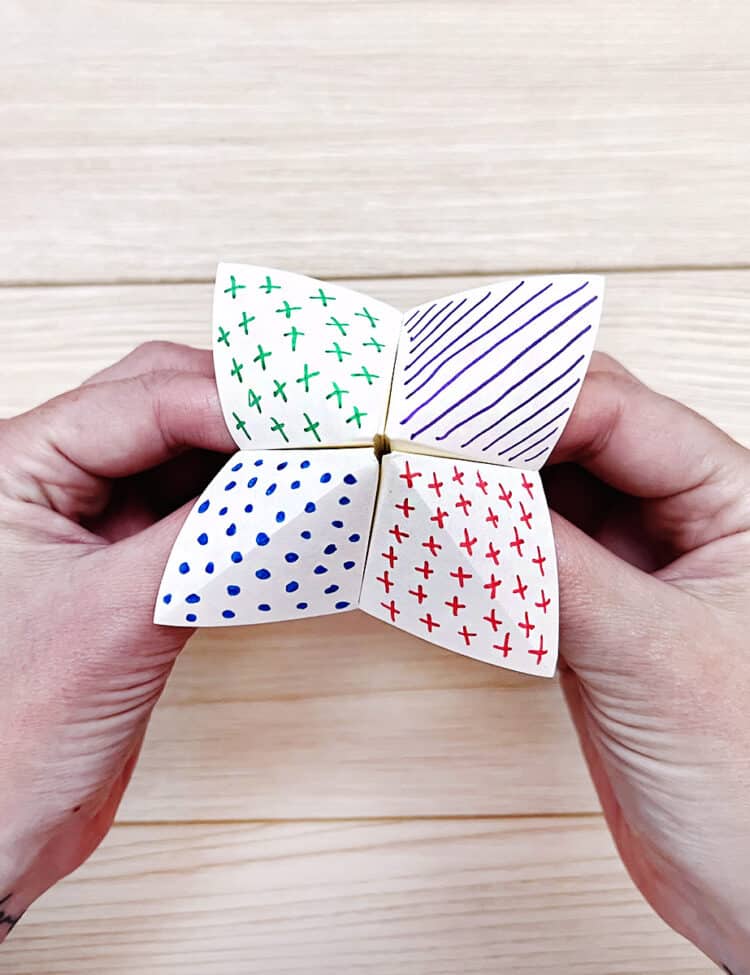 Hands holding a cootie catcher fortune teller.