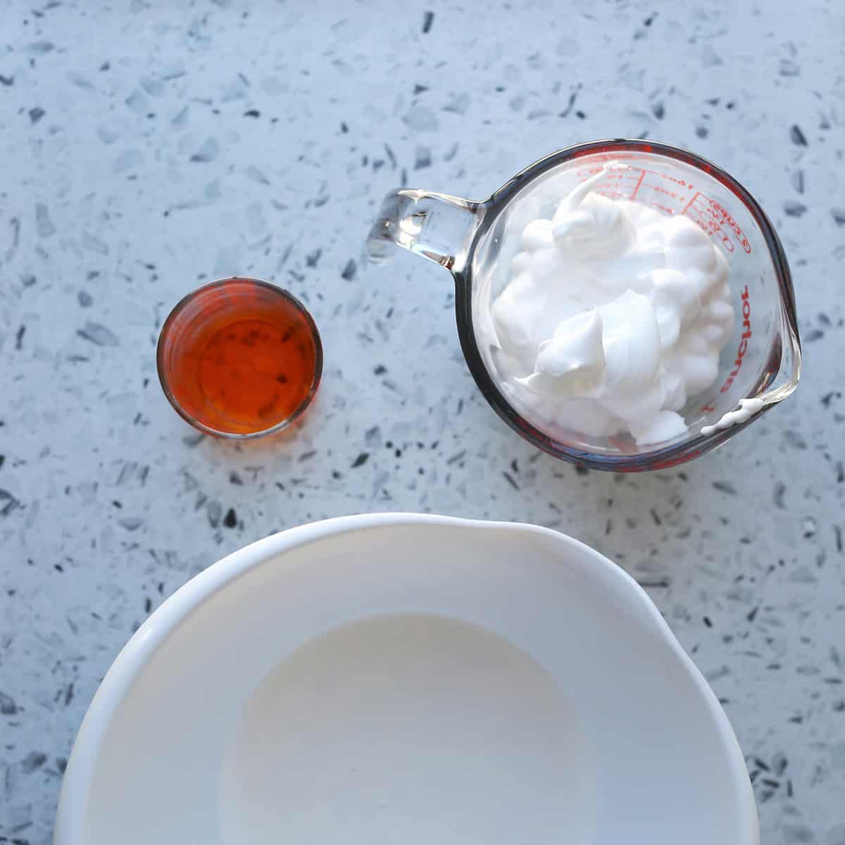 bowl of glue next to glass of dyed food coloring and a measuring cup of shaving cream.