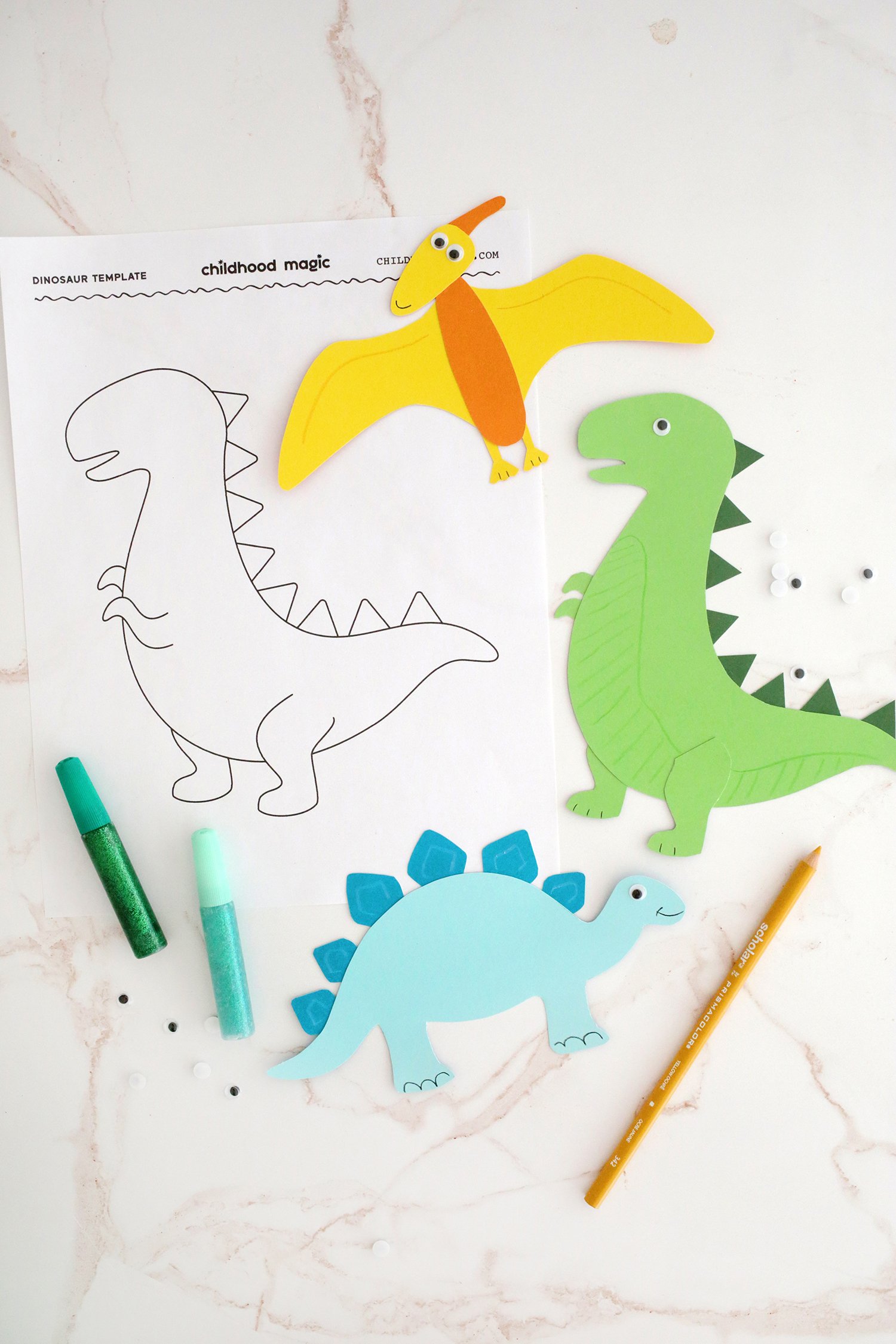 Blue, green and yellow construction paper cut out and made into dinosaur shapes with glitter pens and coloring pencils next to a coloring page. 