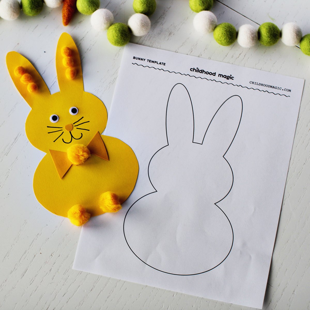 yellow bunny cut out of paper on a table decorated with craft paper, pom poms and googley eyes. A piece of paper with the bunny outline on it. 