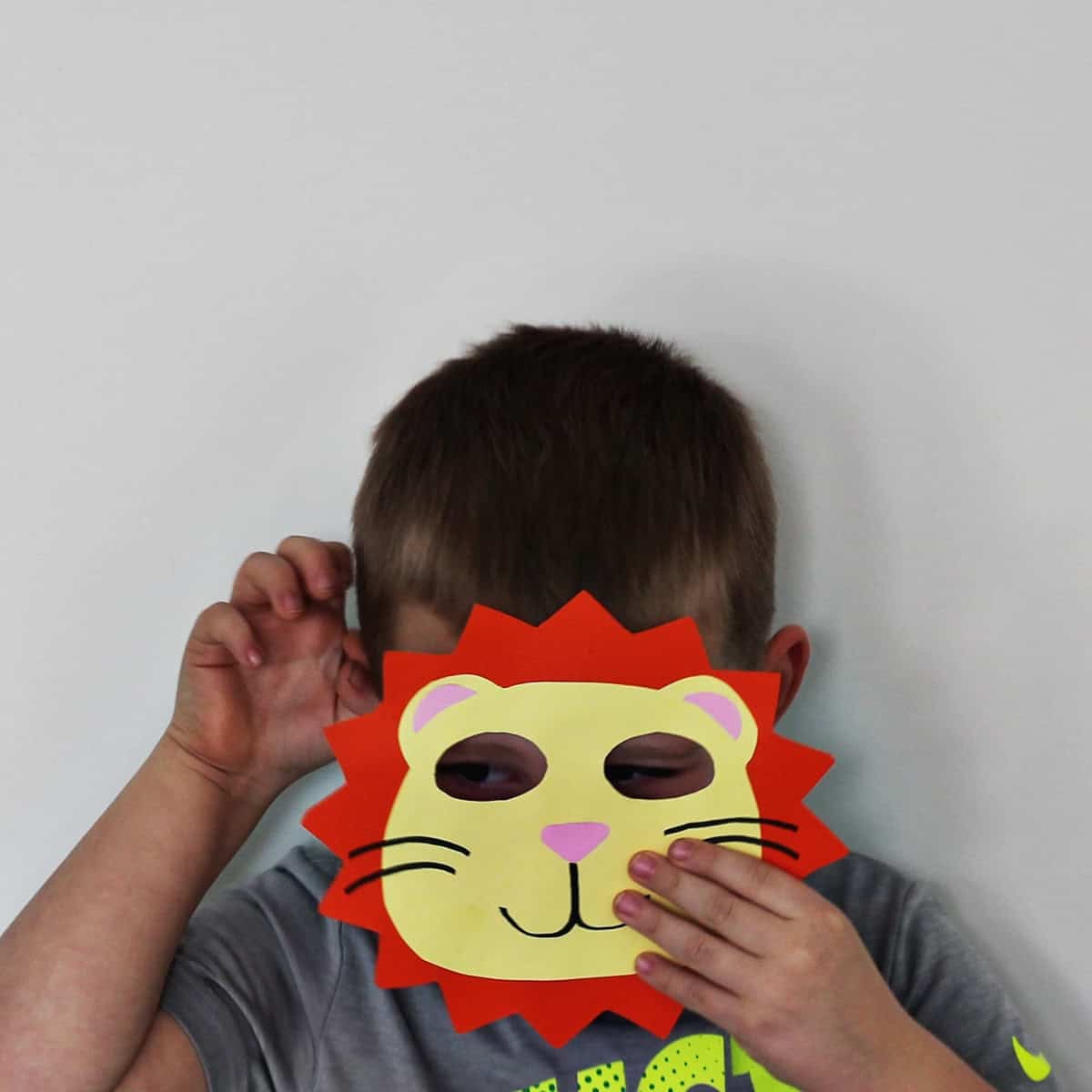 Child holding a lion mask in front of his face while holding up his hand.