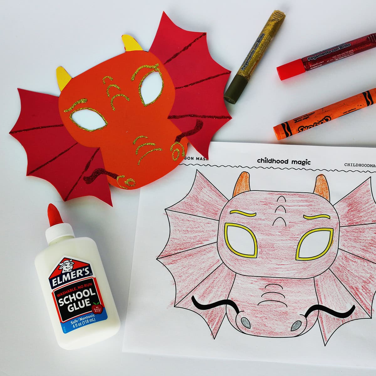 Mask made out of red, orange and yellow cardstock next to a coloring page with the same mask on it. Next to the paper is a bottle of glue, an orange crayon and two glitter pens. 