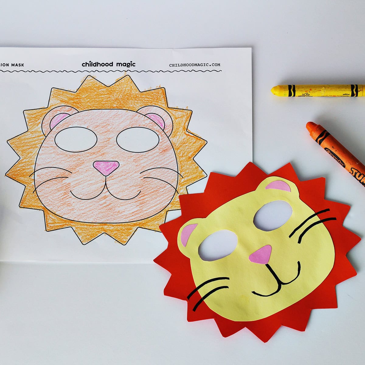 Mask made out of orange, pink and yellow cardstock next to a coloring page with the same mask on it. Next to the paper is a yellow and orange crayon. 