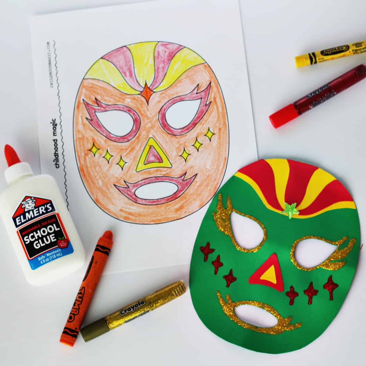 Mask made out of green, red and yellow cardstock next to a coloring page with the same mask on it. Next to the paper is a bottle of glue, crayons and glitter pens. 