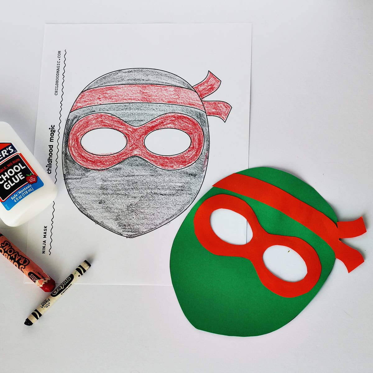 Mask made out of green and orange cardstock next to a coloring page with the same mask on it. Next to the paper is a bottle of glue and a red and black crayon. 