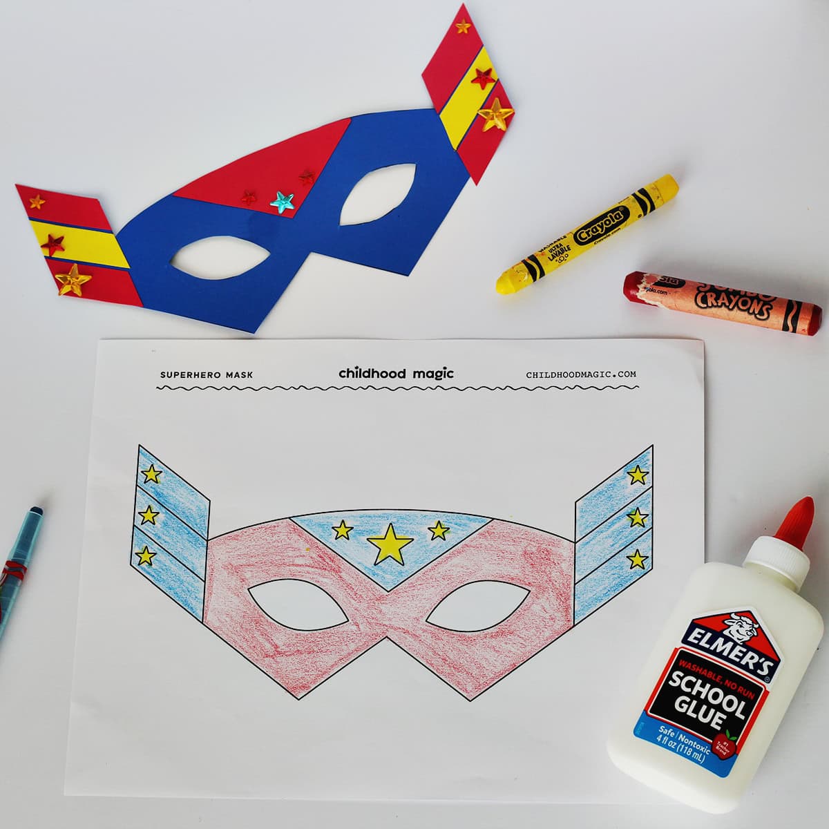 Mask made out of blue, red and yellow cardstock next to a coloring page with the same mask on it. Next to the paper is a bottle of glue and a red and yellow crayon. 