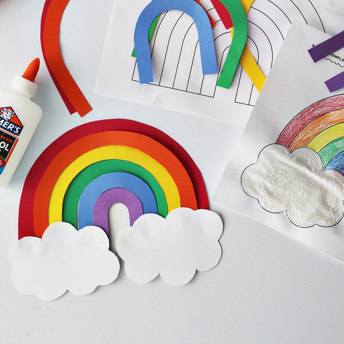 cardstock cut and glued together to make a rainbow next to a rainbow coloring page and a bottle of glue on a white table.