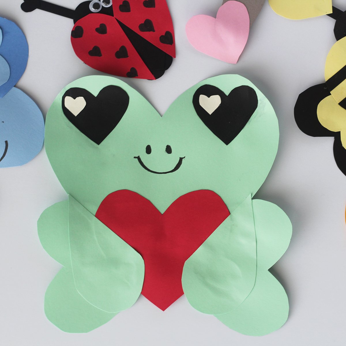 Green construction paper in heart shapes glued together to make a frog holding ared construction heart.