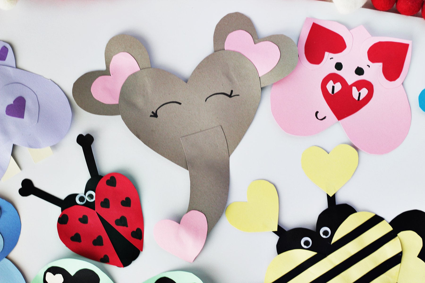 Grey cardstock paper cut into hearts and glued together to make an elepehant face and a strip of grey paper as the trunk. Elephant is next to other cardstock animals in pink, red, yellow, green and purple colors. 