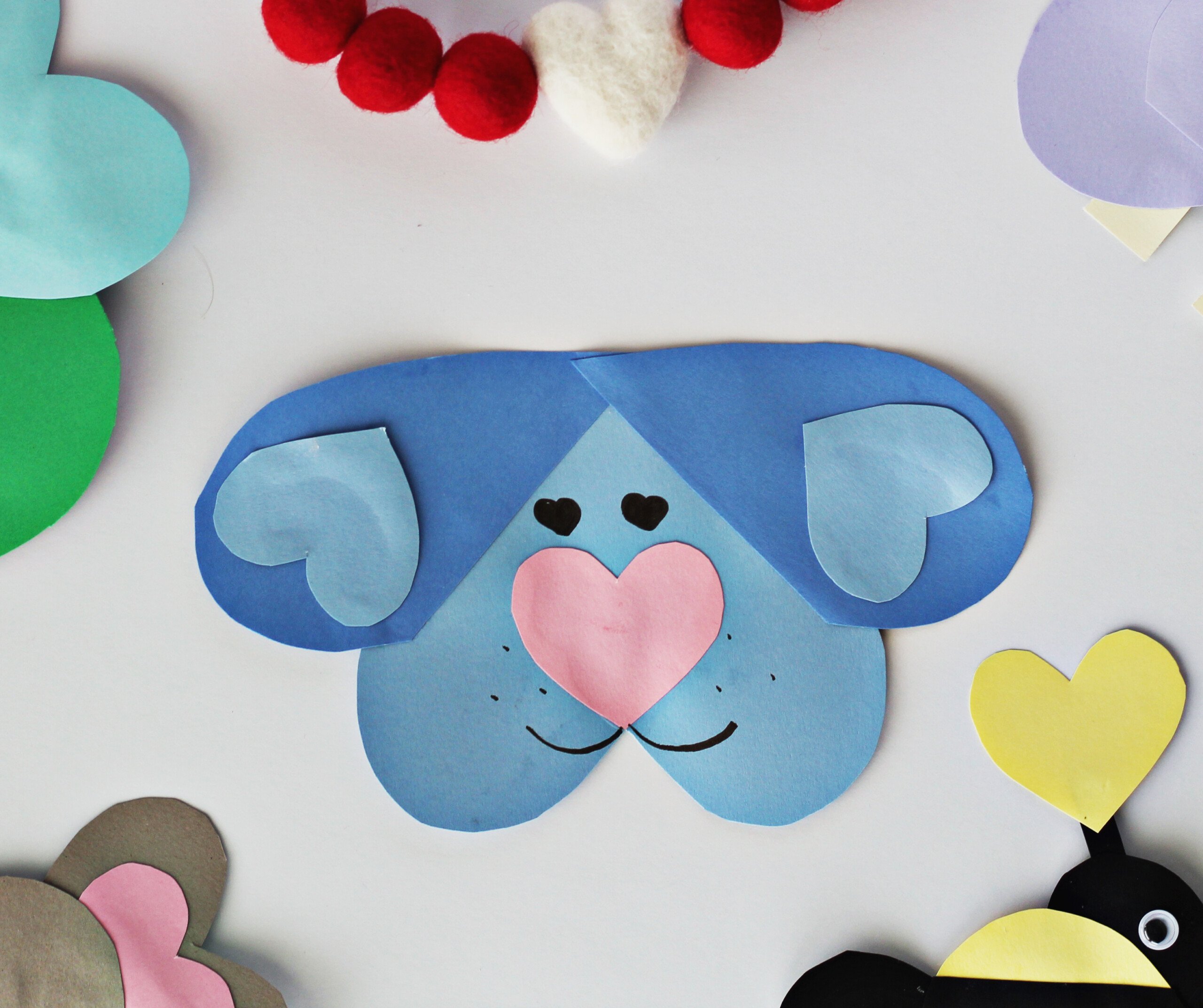 Blue cardstock cut into heart shapes and glued together to make a dog face and ears. Pink cardstock is cut out and glued on as the nose. 