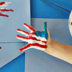 Child's hand painted with red and white stripes and a blue area to make an American flag.