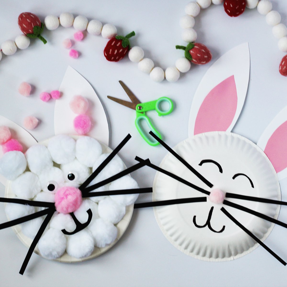 Two bunny faces made from paper plates with cardstock and pom poms. Next to the plates are a pair of green kids scissors.