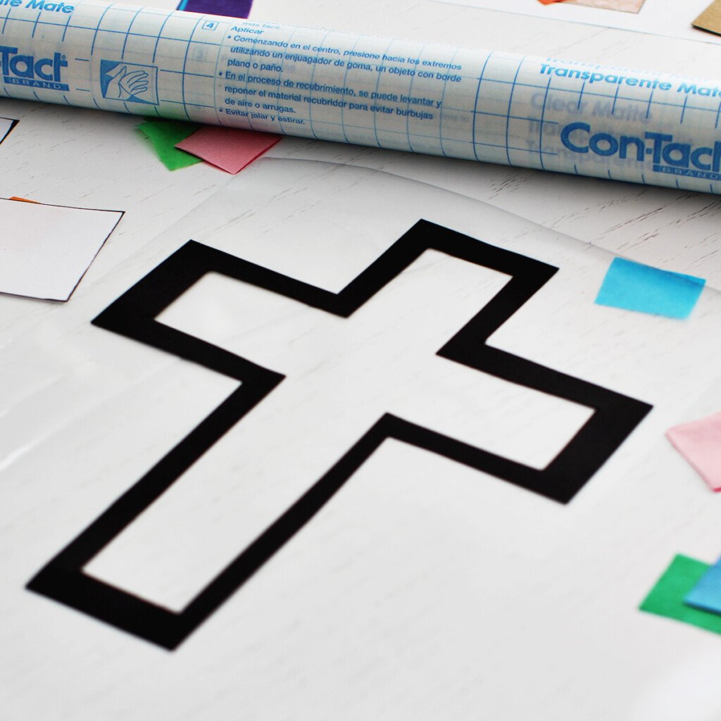 Cross outline added to contact paper next to a roll of contact paper with colored tissue paper on the table.