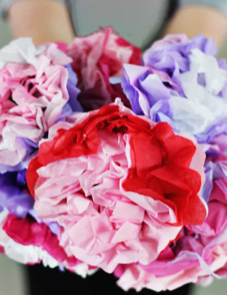 Child holding a bouquet made up of flowers made from tissue paper in red, pink, purple and white.