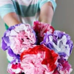Child holding a bouquet made up of flowers made from tissue paper in red, pink, purple and white.