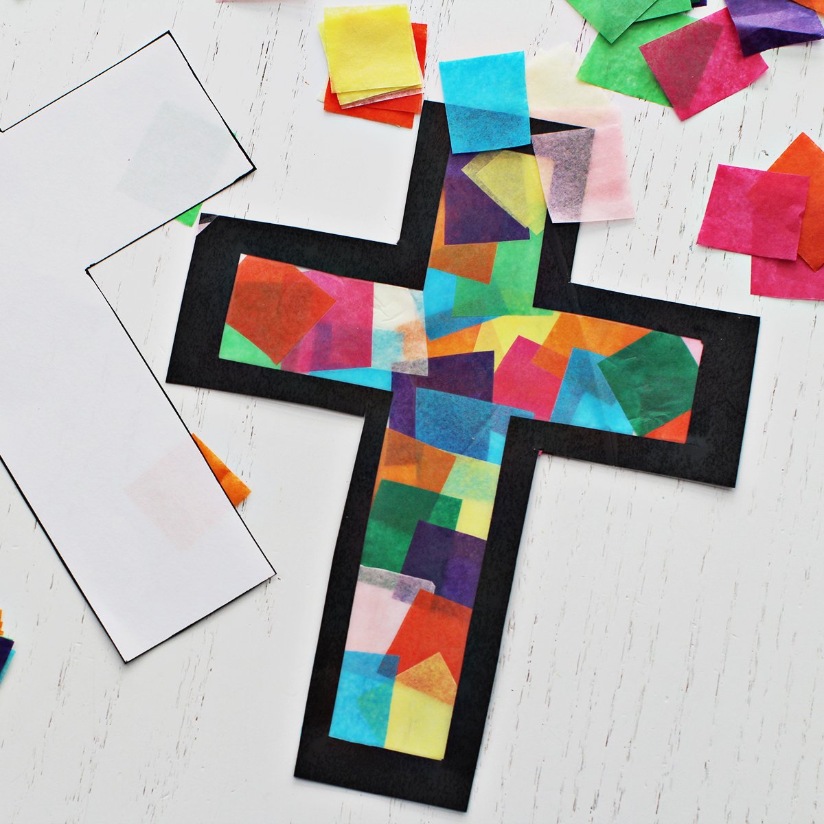 Colored tissue paper added to a cross outline on contact paper to make a suncatcher or stained glass cross craft.