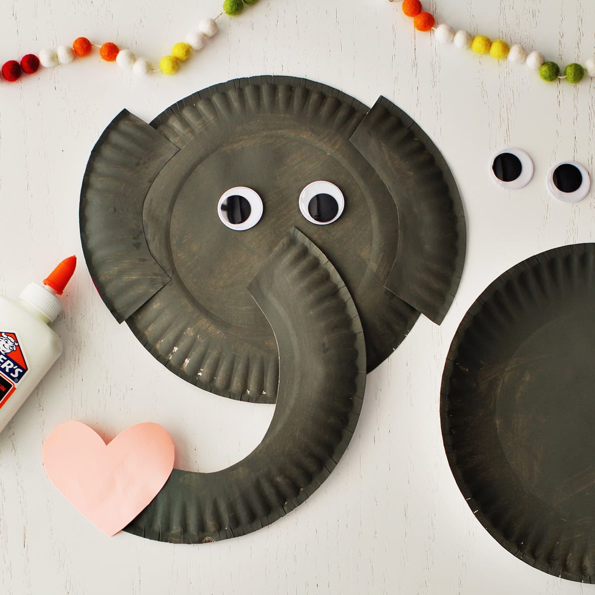 Googley eyes and a pink cardstock heart glued onto pieces of paper plates painted grey to make an elephant craft.
