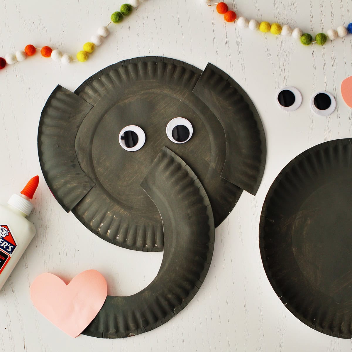 gray painted paper plate cut and glued to another gray paper plate with a pink cardstock heart attached to make an elepeahnt from paper plates.