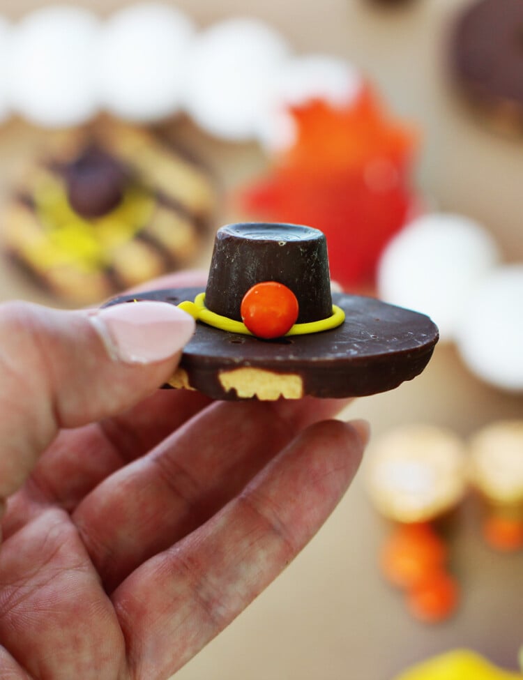 Hand holding a cookie that's made up of a fudge stripe cookie, a rolo, yellow icing and an orange mini m&m.