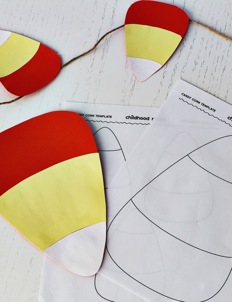 outline of a candy corn next to a cut out candy corn made from orange, yellow and white cardstock. Smaller cut out candy corn candies are above the large one.