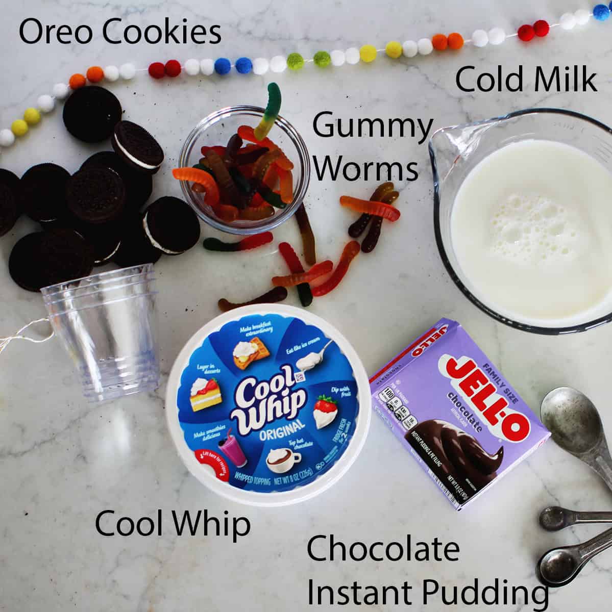 Oreo cookies, a bowl of hummy worms, a bowl of cold milk, a continer of cool whip and a container of chocolate instant pudding.