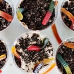 4 plastic cups filled with pudding, crushed oreos and gummy worms for a dessert.