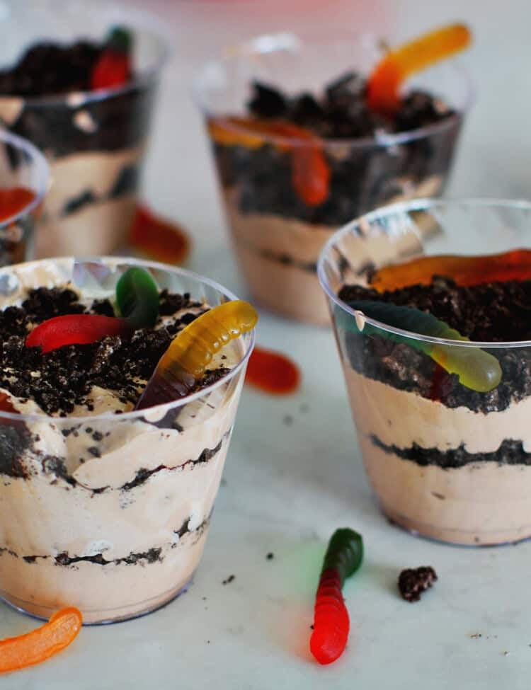 4 plastic cups filled with pudding, crushed oreos and gummy worms for a dessert.