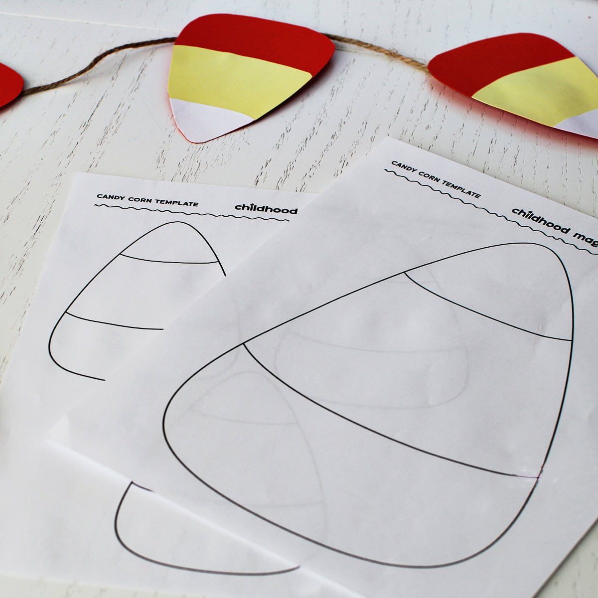 White paper with a black outline of a large candy corn on it. Next to the template is a cut out candy corn garland.