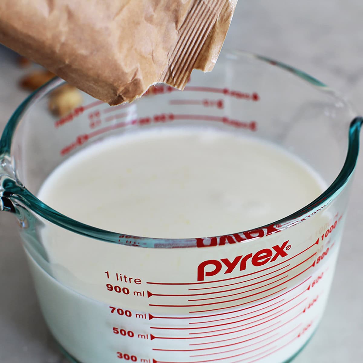 Liquid measuring cup filled with milk with pudding mix being added to it.