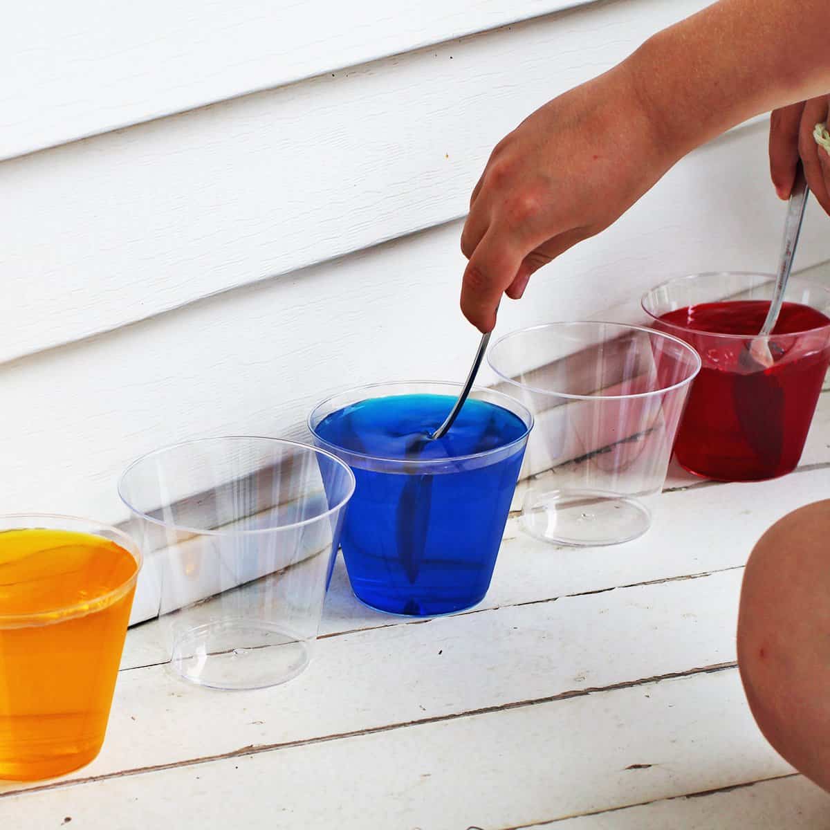 Kid stirring food coloring into cup of water.