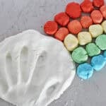 Handprint in white cloud dough next to balls of homemade dough in rainbow colors.